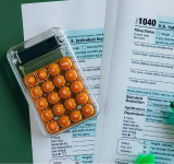 Una calculadora y dos resaltadores descansan sobre formularios completos del impuesto sobre la renta individual de EE. UU. (1040), reflejando los retos de declarar impuestos como músico independiente, sobre una superficie verde.