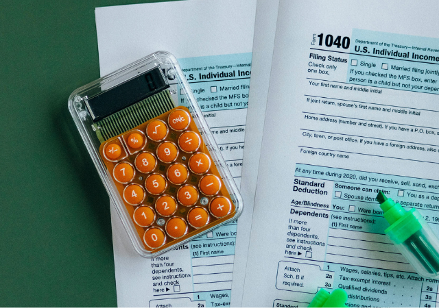 Una calculadora y dos resaltadores descansan sobre formularios completos del impuesto sobre la renta individual de EE. UU. (1040), reflejando los retos de declarar impuestos como músico independiente, sobre una superficie verde.