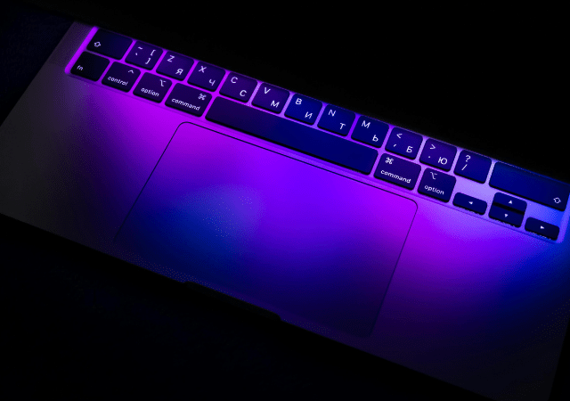 El teclado y el trackpad de una laptop, iluminados por luces moradas y azules, crean una imagen sinfónica con caracteres cirílicos rusos danzando elegantemente sobre las teclas.