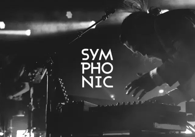Entre luces deslumbrantes, un músico se alza en silueta frente a un fondo electrizante con el logo de “SYMPHONIC”, cautivando al público con cada nota. Esta actuación hipnotizante también funciona como una gran promoción de sus más recientes paisajes sonoros transformadores.