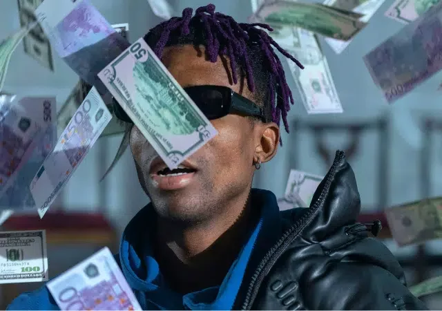 Una persona con gafas de sol y chaqueta oscura está rodeada de billetes de varias denominaciones cayendo a su alrededor, ilustrando el caos que puede surgir de no llevar un presupuesto.