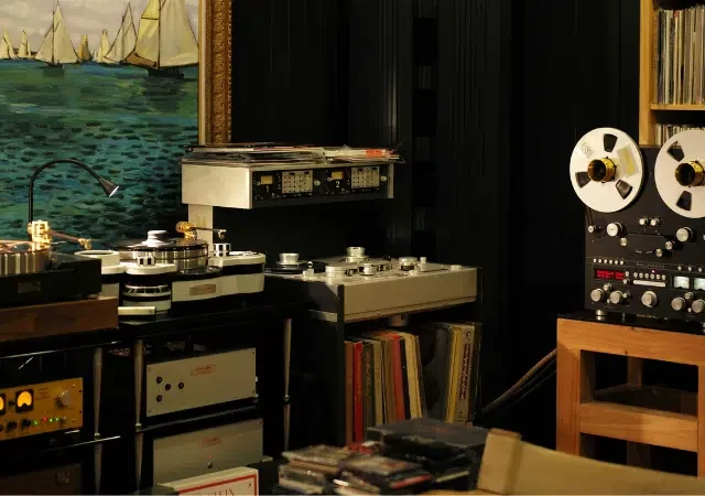 Habitación con equipo de audio vintage, incluidos grabadoras de carrete, tornamesas y amplificadores — un paraíso para los amantes de la música física — con estantes de vinilos y una gran pintura de veleros en la pared.