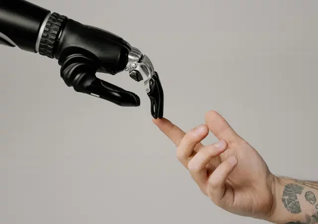 Una mano robótica y una mano humana se extienden una hacia la otra, con los dedos casi tocándose sobre un fondo sencillo, simbolizando la intersección entre tecnología y humanidad en una escena que recuerda a imágenes icónicas del copyright.