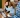 Una persona con una camisa de cuadros usa un smartphone y una laptop, posiblemente revisando Amazon Music Insights, mientras otras dos personas con laptops conversan en el fondo.