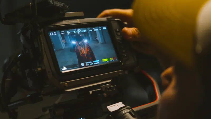 Una persona opera una cámara de video en sincronía perfecta, capturando imágenes de alguien en un pasillo, mostradas en la pantalla del monitor de la cámara.