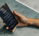 Una persona sostiene un smartphone que muestra el sitio web de ChatGPT sobre una mesa con patrones geométricos, ilustrando cómo ChatGPT se integra perfectamente en la vida cotidiana.