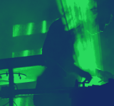 Un músico actuando como DJ en una habitación oscura con luces verdes.