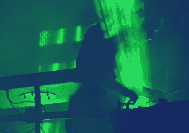 Un músico actuando como DJ en una habitación oscura con luces verdes.