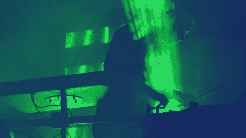 Un músico actuando como DJ en una habitación oscura con luces verdes.