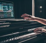 Una persona toca un teclado electrónico con un portátil encima, mostrando el software de producción musical de Meta en la pantalla, en un entorno tenue.