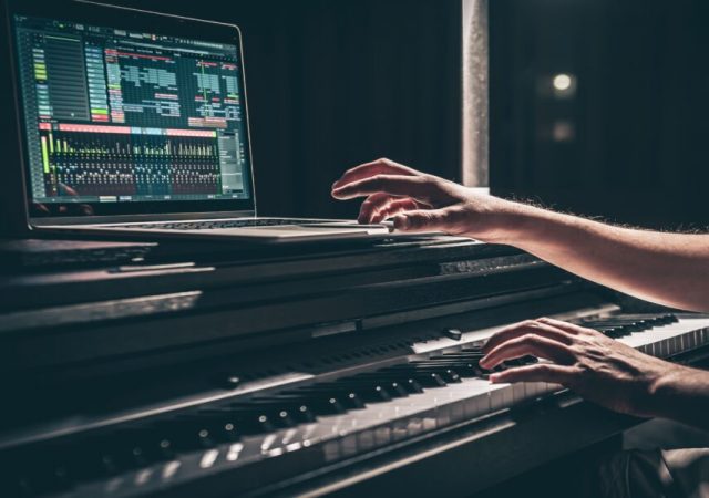 Una persona toca un teclado electrónico con un portátil encima, mostrando el software de producción musical de Meta en la pantalla, en un entorno tenue.