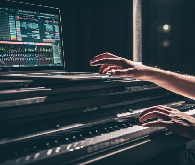 Una persona toca un teclado electrónico con un portátil encima, mostrando el software de producción musical de Meta en la pantalla, en un entorno tenue.