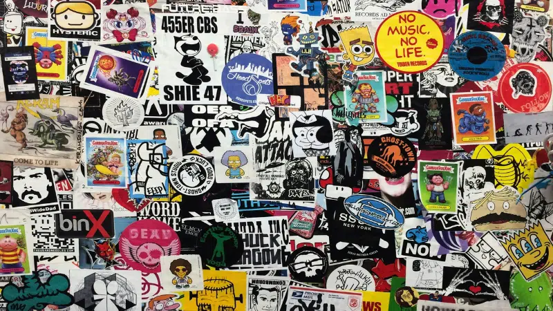 Una pared densamente cubierta de stickers coloridos variados, con diferentes personajes, logos, slogans de marcas registradas y diseños artísticos superpuestos entre sí.