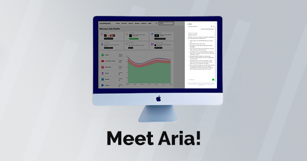 Un iMac muestra un panel con gráficos y métricas junto a un documento de texto, destacando soporte con IA. Las palabras “Meet Aria!” aparecen debajo de la pantalla.