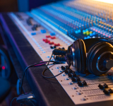 Unos audífonos descansan sobre una gran consola de mezcla de audio con numerosos botones, perillas y faders en un estudio de grabación, donde ingenieros de sonido gestionan datos de audio para lograr grabaciones perfectas.