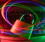 Un candado descansa sobre el teclado de un laptop con trazos de luz roja y azul girando, representando la ciberseguridad, la protección de datos y la seguridad del copyright en el mundo digital.