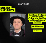 Una persona con un sombrero negro de ala ancha, corbatín y saco posa frente a un fondo con símbolos dorados de gramófonos.