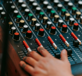 Una mano ajusta sliders y perillas en una consola de mezcla de audio impulsada por IA, con varios controles y botones de colores visibles.