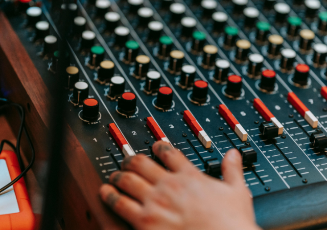 Una mano ajusta sliders y perillas en una consola de mezcla de audio impulsada por IA, con varios controles y botones de colores visibles.