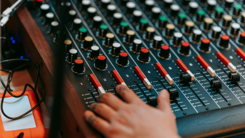 Una mano ajusta sliders y perillas en una consola de mezcla de audio impulsada por IA, con varios controles y botones de colores visibles.