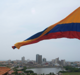 Una gran bandera colombiana ondea sobre el paisaje urbano, donde edificios modernos e históricos se alzan bajo un cielo nublado: una vista inspiradora, especialmente durante Circulart, cuando la creatividad llena el ambiente.