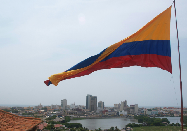 Una gran bandera colombiana ondea sobre el paisaje urbano, donde edificios modernos e históricos se alzan bajo un cielo nublado: una vista inspiradora, especialmente durante Circulart, cuando la creatividad llena el ambiente.