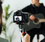 Una persona graba un video de YouTube de alguien tocando una guitarra acústica usando una cámara DSLR sobre un trípode.
