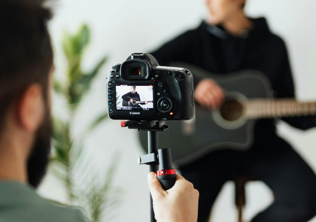 Una persona graba un video de YouTube de alguien tocando una guitarra acústica usando una cámara DSLR sobre un trípode.