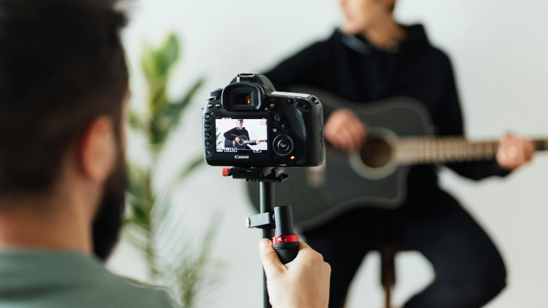 Una persona graba un video de YouTube de alguien tocando una guitarra acústica usando una cámara DSLR sobre un trípode.